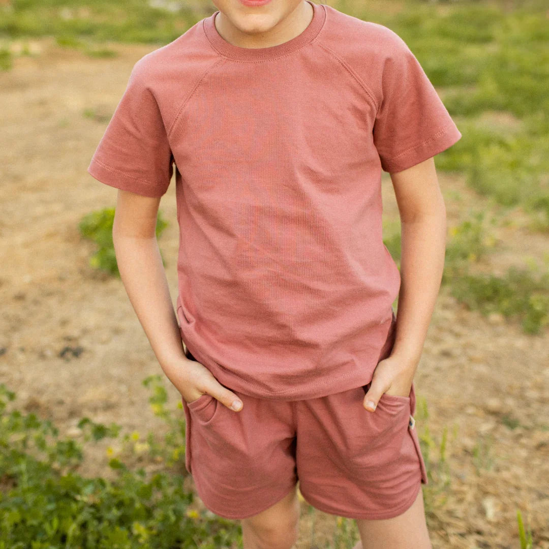 Kid in dusty rose organic cotton tee and shorts, hands in pockets outdoors