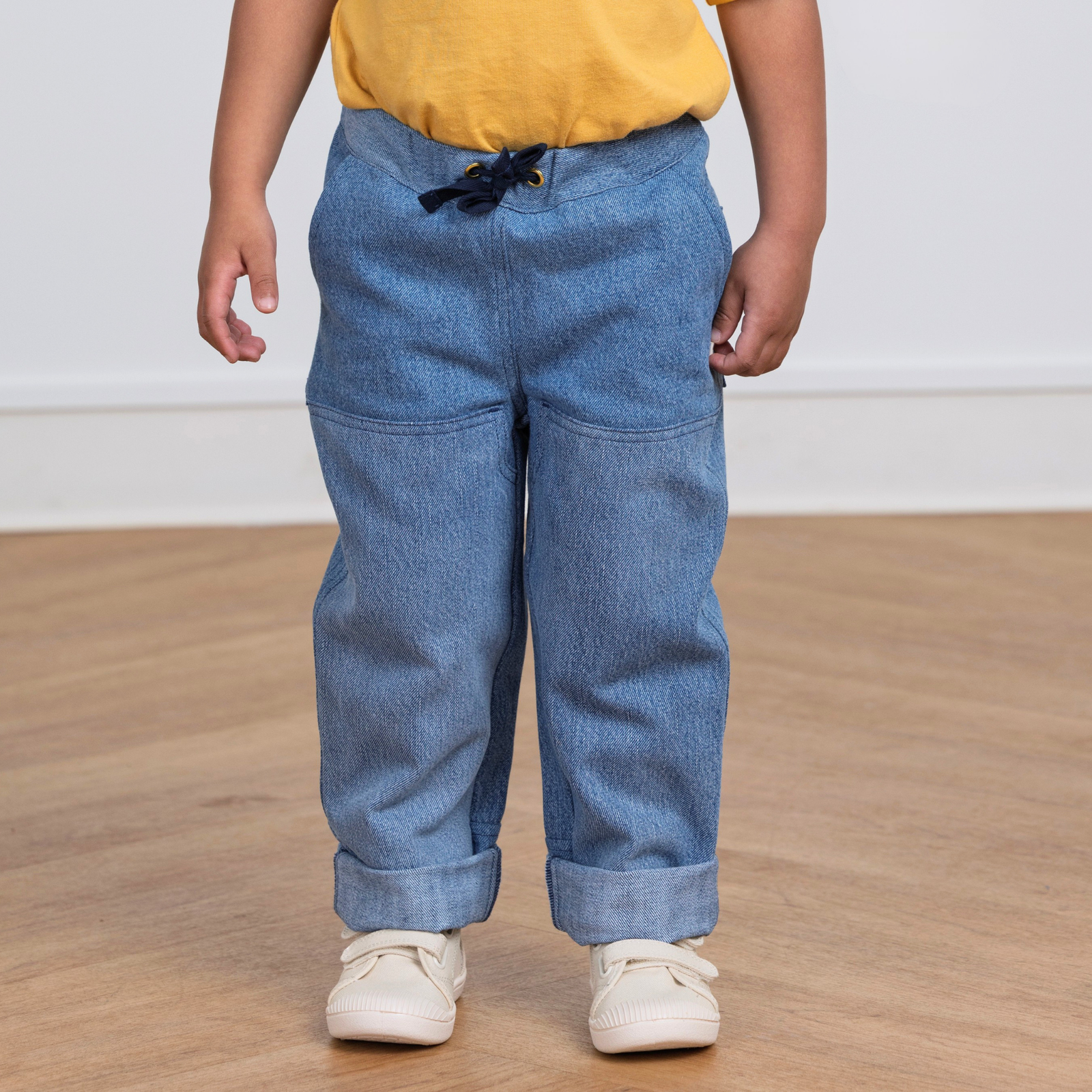 Kid wearing durable blue upcycled denim pants with drawstring waist, cuffed hems, and side pockets for active play