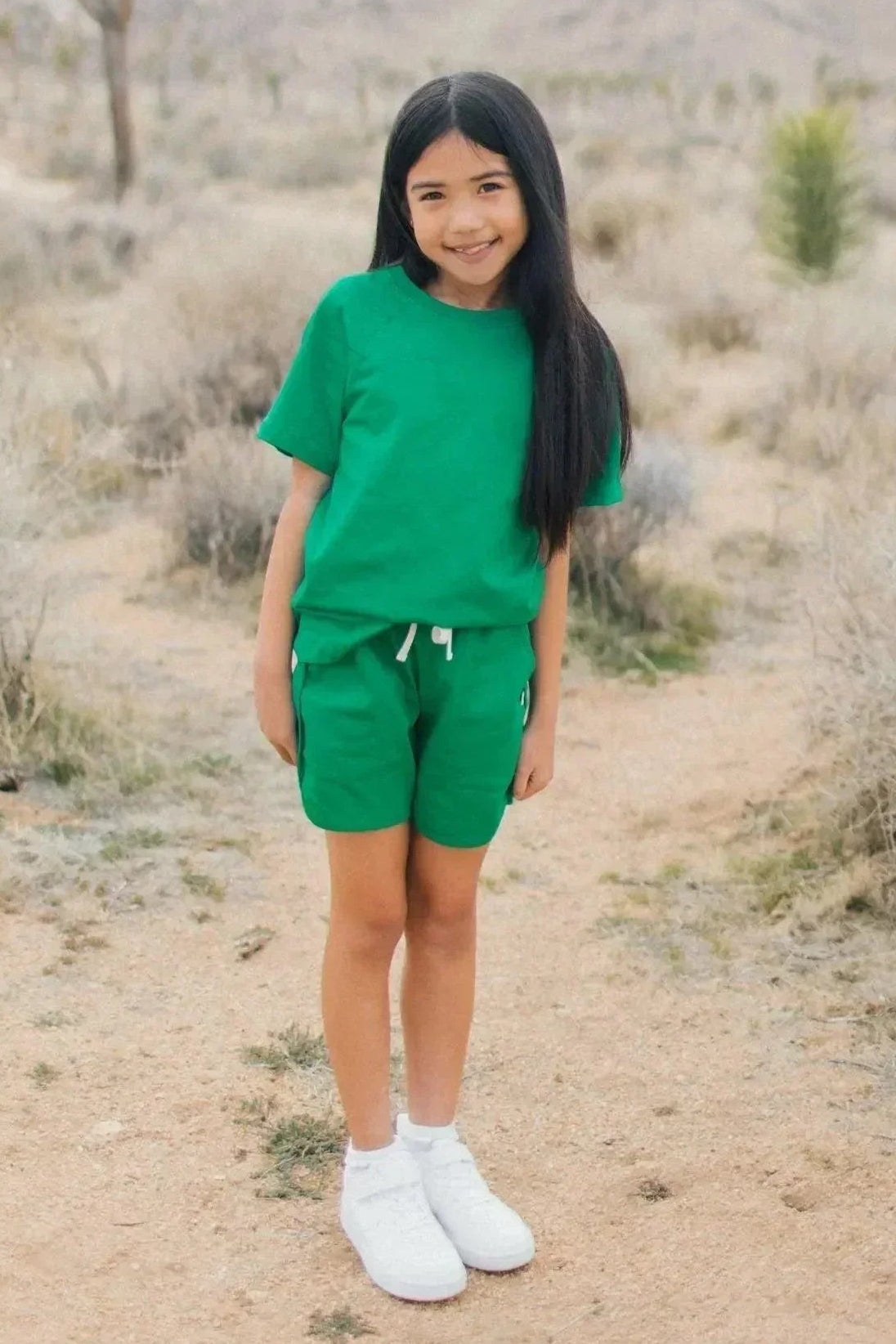 Smiling girl in green Jackalo shorts and t-shirt, standing outdoors in a desert landscape