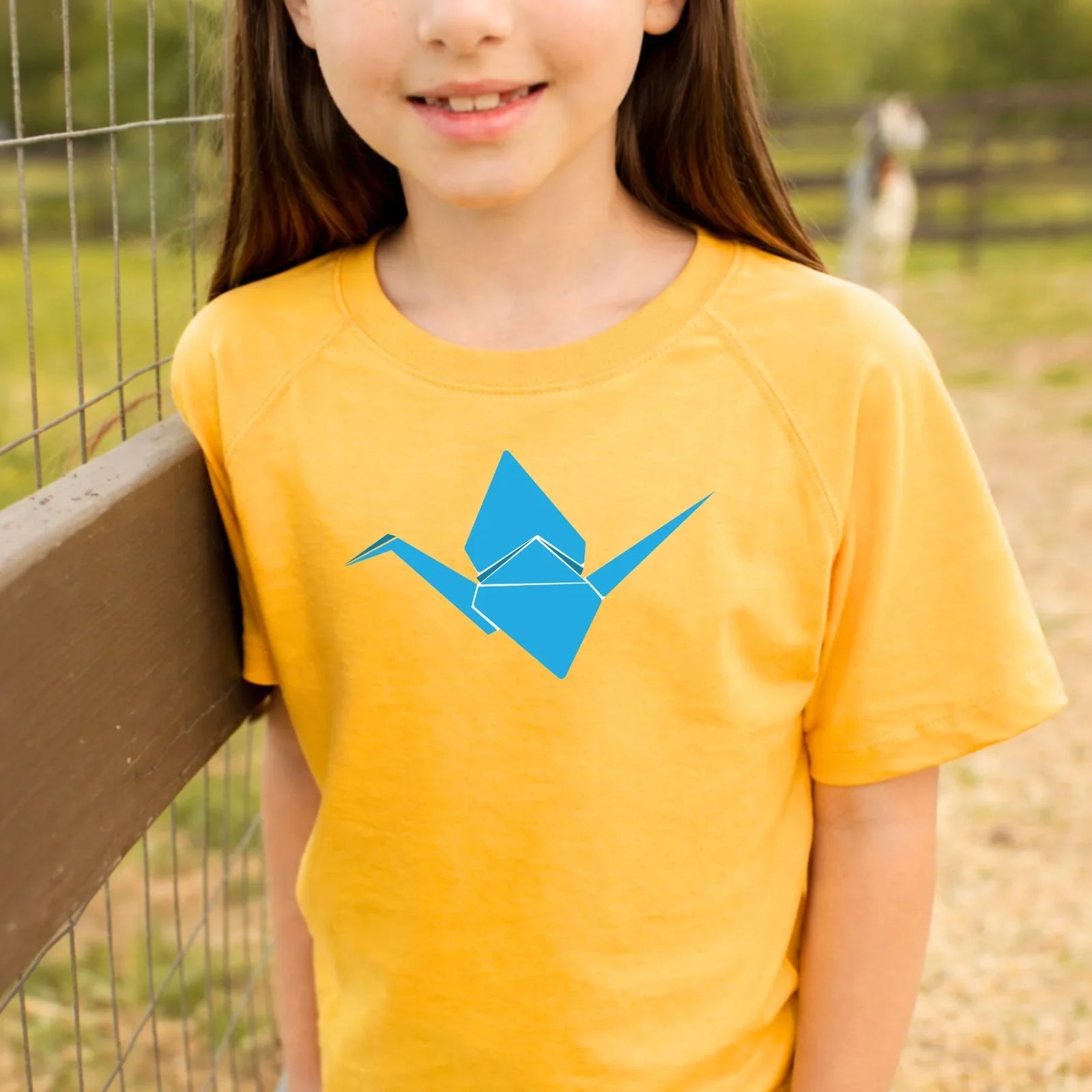 Girl wearing yellow kids tee with blue origami crane graphic, perfect for active play outdoors