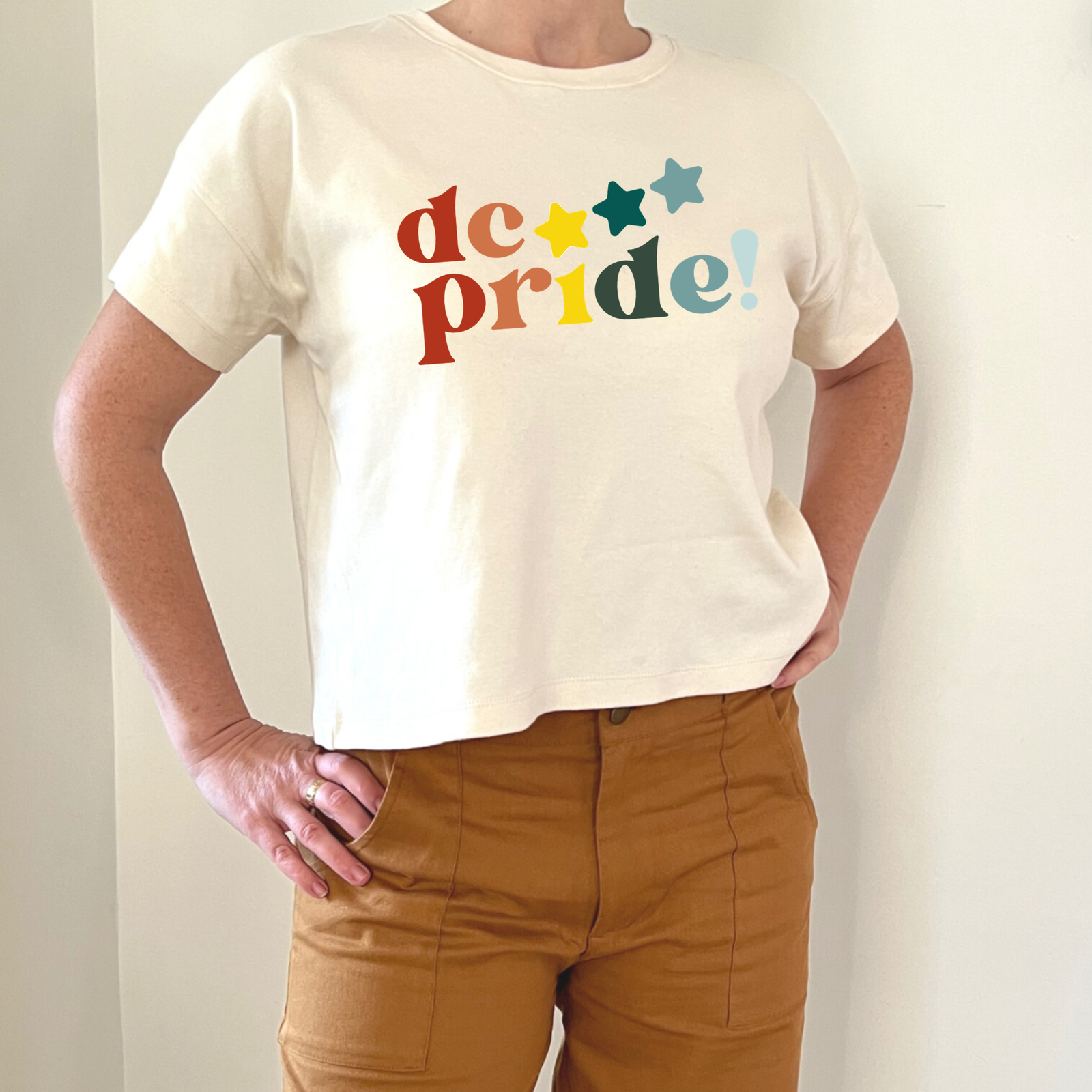 Cream crop tee with colorful 'dc pride!' text and stars, paired with tan pants