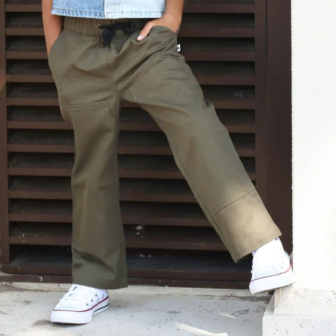 Child wearing Jackalo dark olive Jules pants with white sneakers, standing outdoors