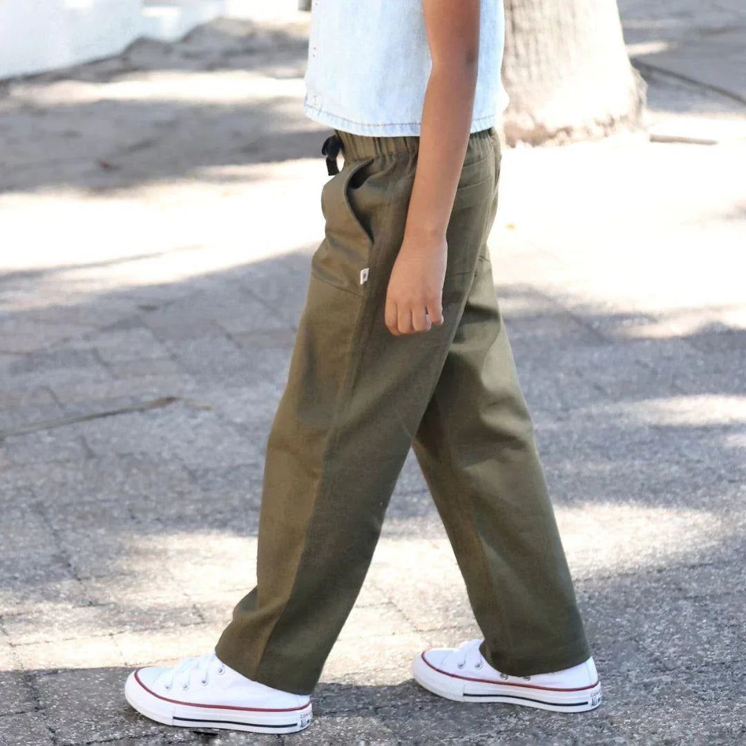 Child wearing Jackalo dark olive sustainable pants outdoors, white sneakers, and light vest