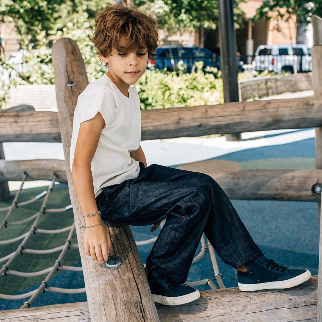 Child wearing Jackalo sustainable jeans and a white shirt on a playground, outdoors.