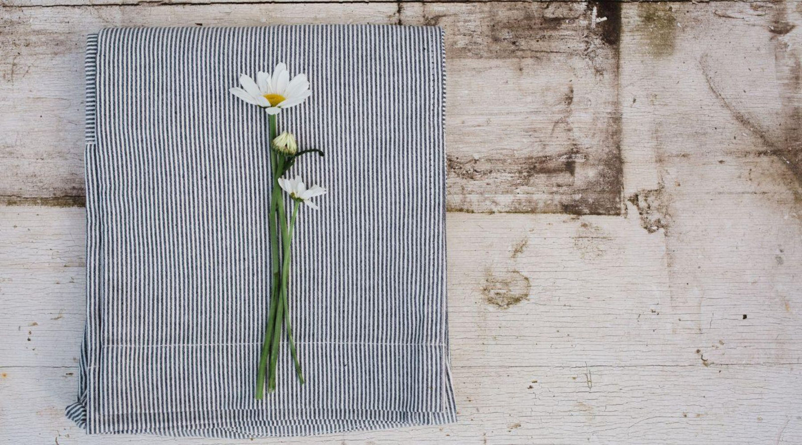 Blue striped textile with daisies on rustic wood, sustainable kids clothing concept by Jackalo
