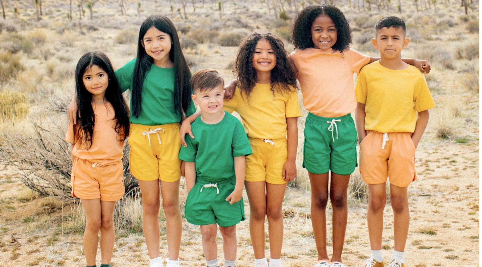 Diverse group of kids in colorful Jackalo sustainable clothing posing outdoors in nature.
