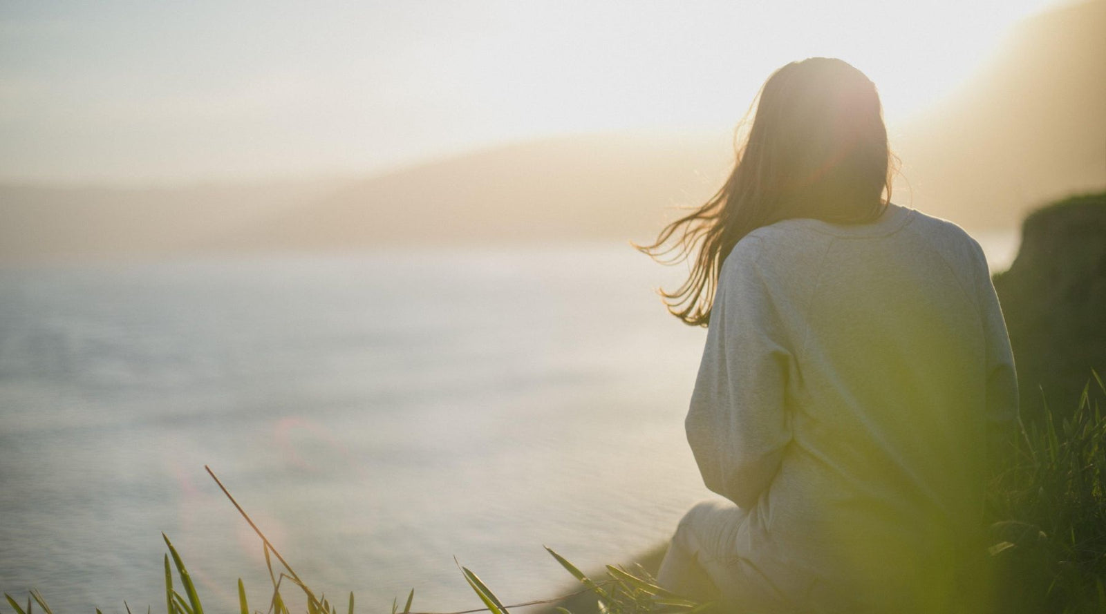 a woman sitting on the rock admiring the ocean