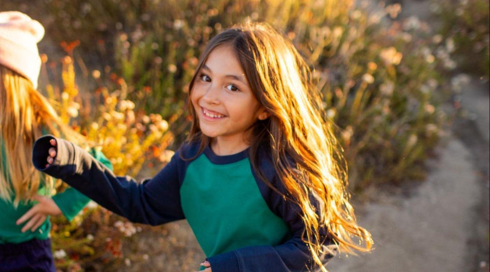 Smiling girl in green Jackalo raglan sweatshirt outdoors on a sunny trail, sustainable kidswear