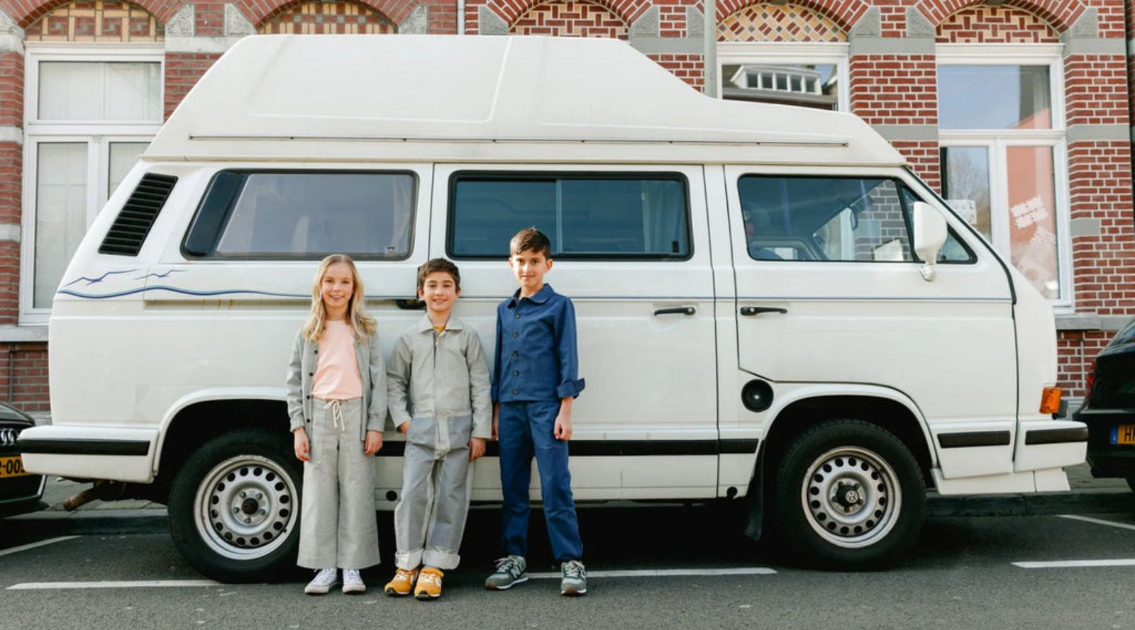 three kids smiling and standing beside a white van