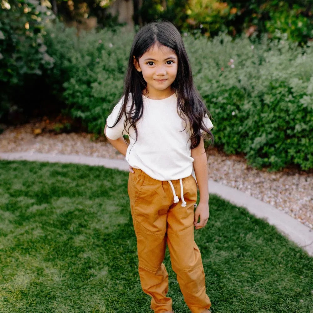 A girl wearing a white shirt and orange pants standing in a backyard