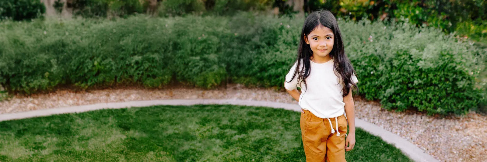 A girl wearing a white shirt and orange pants standing in a backyard