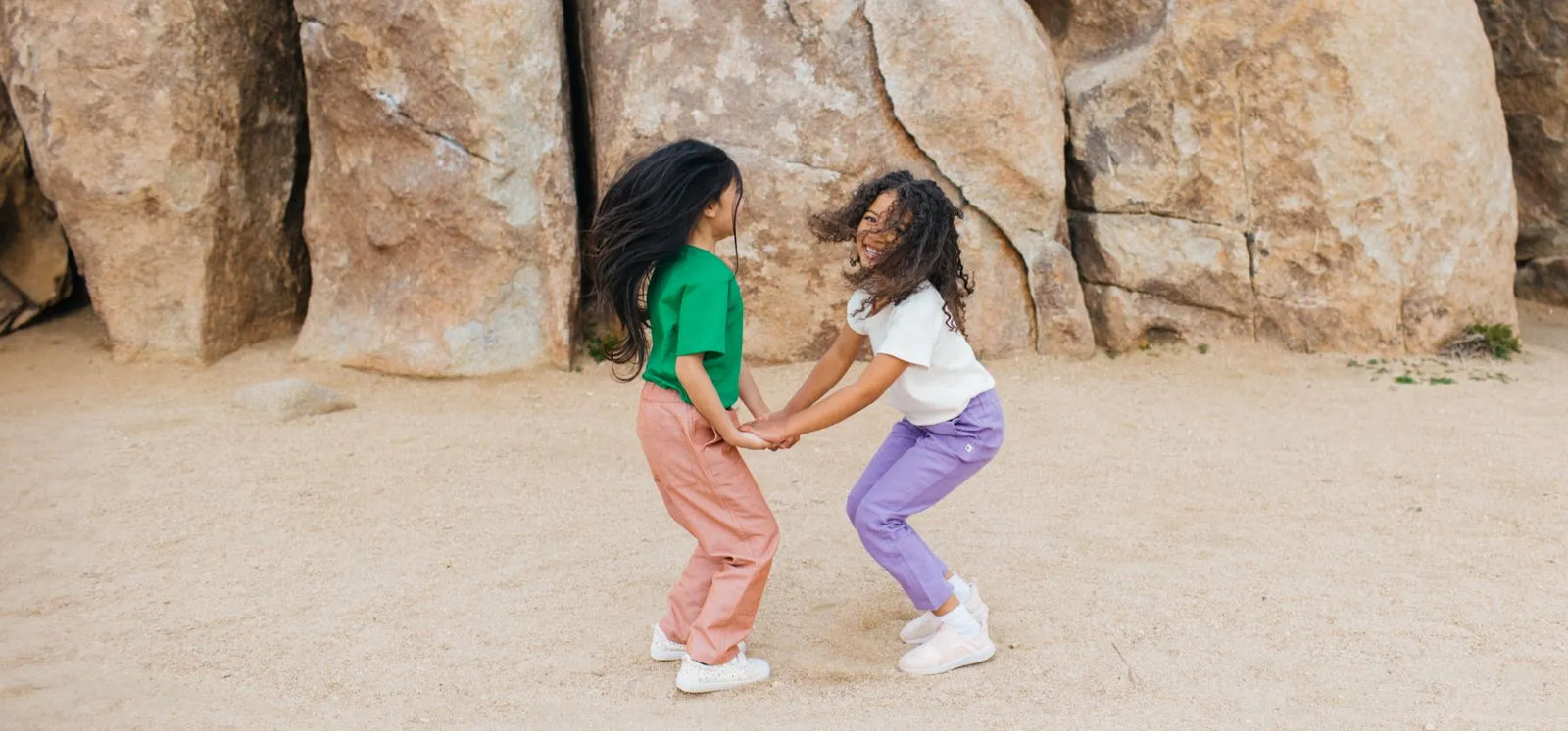 Two girls holding hands jumping in the desert
