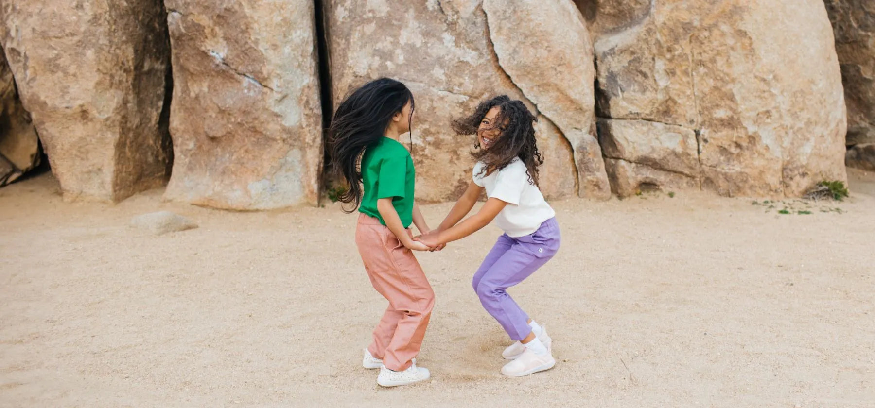 Two girls holding hands jumping in the desert