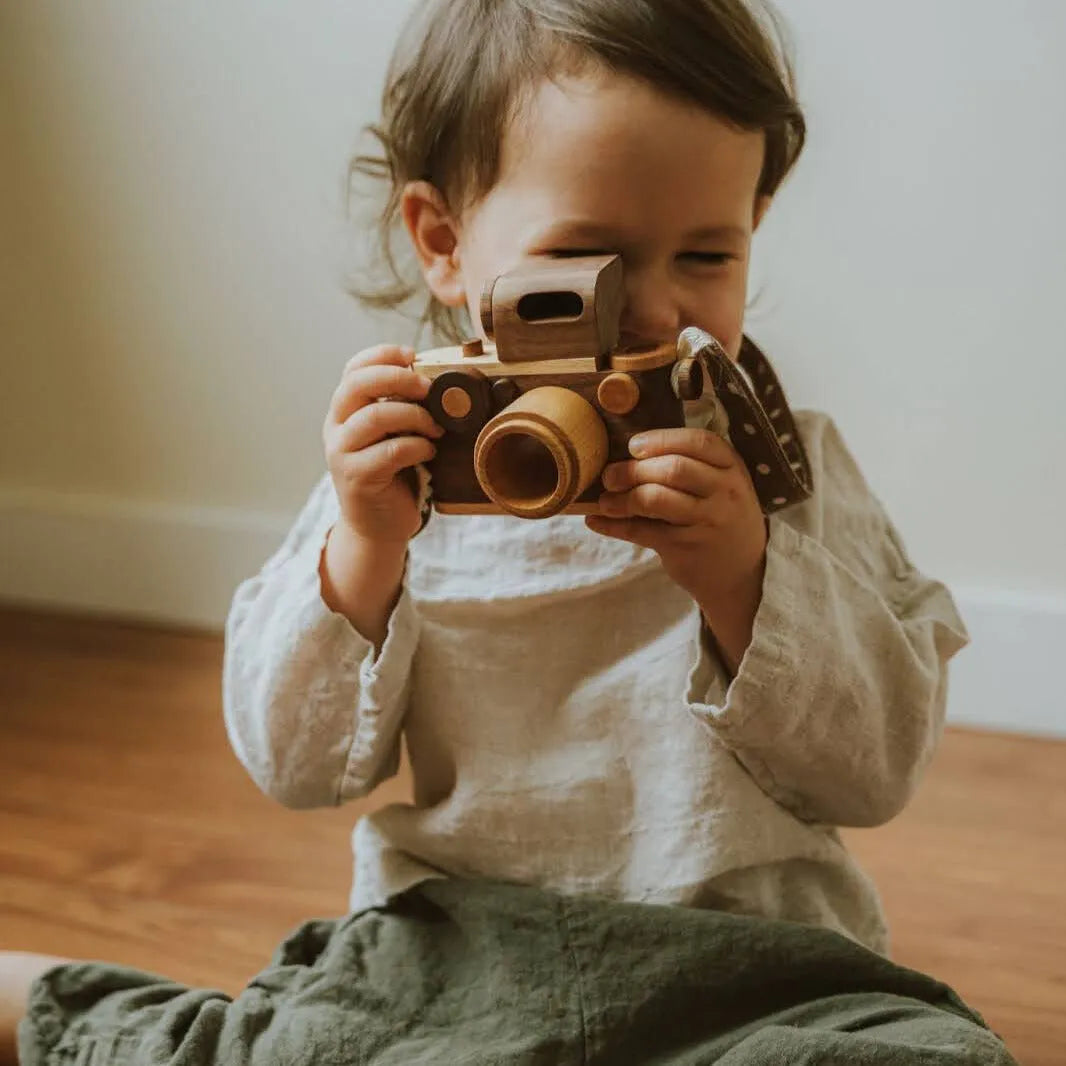 A young child joyfully holding a wooden camera