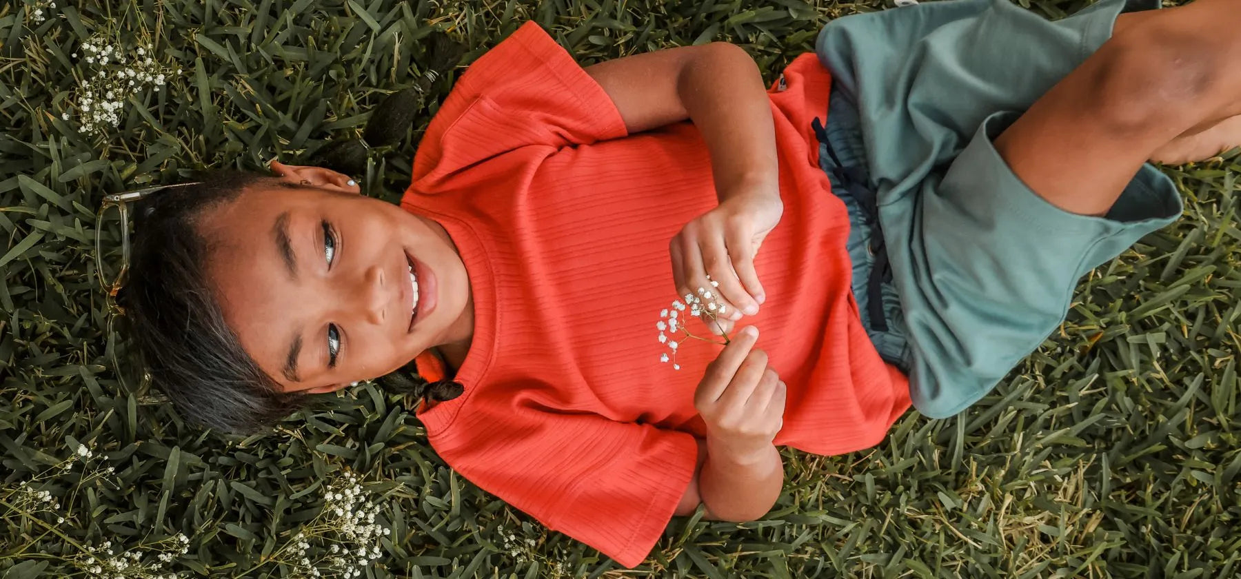 Girl in red shirt and teal shorts laying on grass