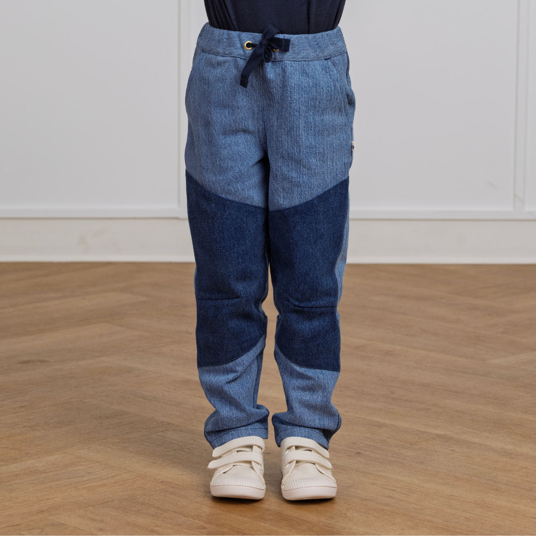 Kids' two-tone denim joggers with drawstring waist, paired with white sneakers on wood floor