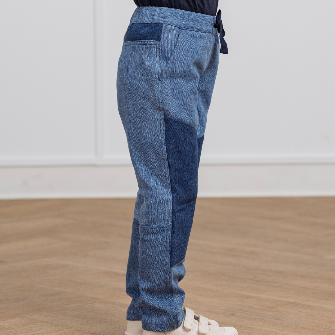 Kids' two-tone denim joggers with drawstring waist, paired with white sneakers on wood floor