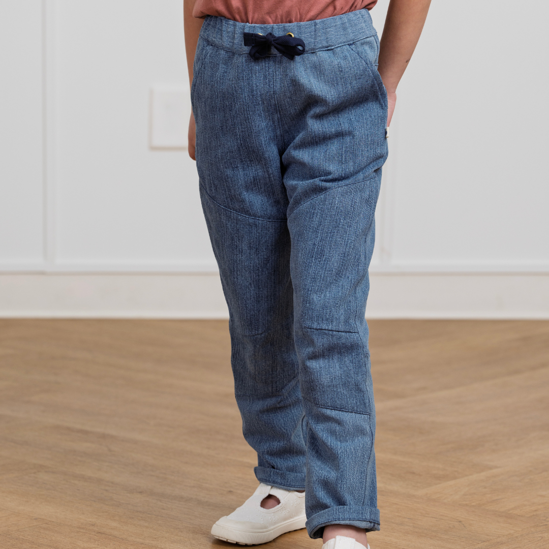 Kids' blue denim-style pants with drawstring waist, cuffed hems, and side pockets, paired with white sneakers