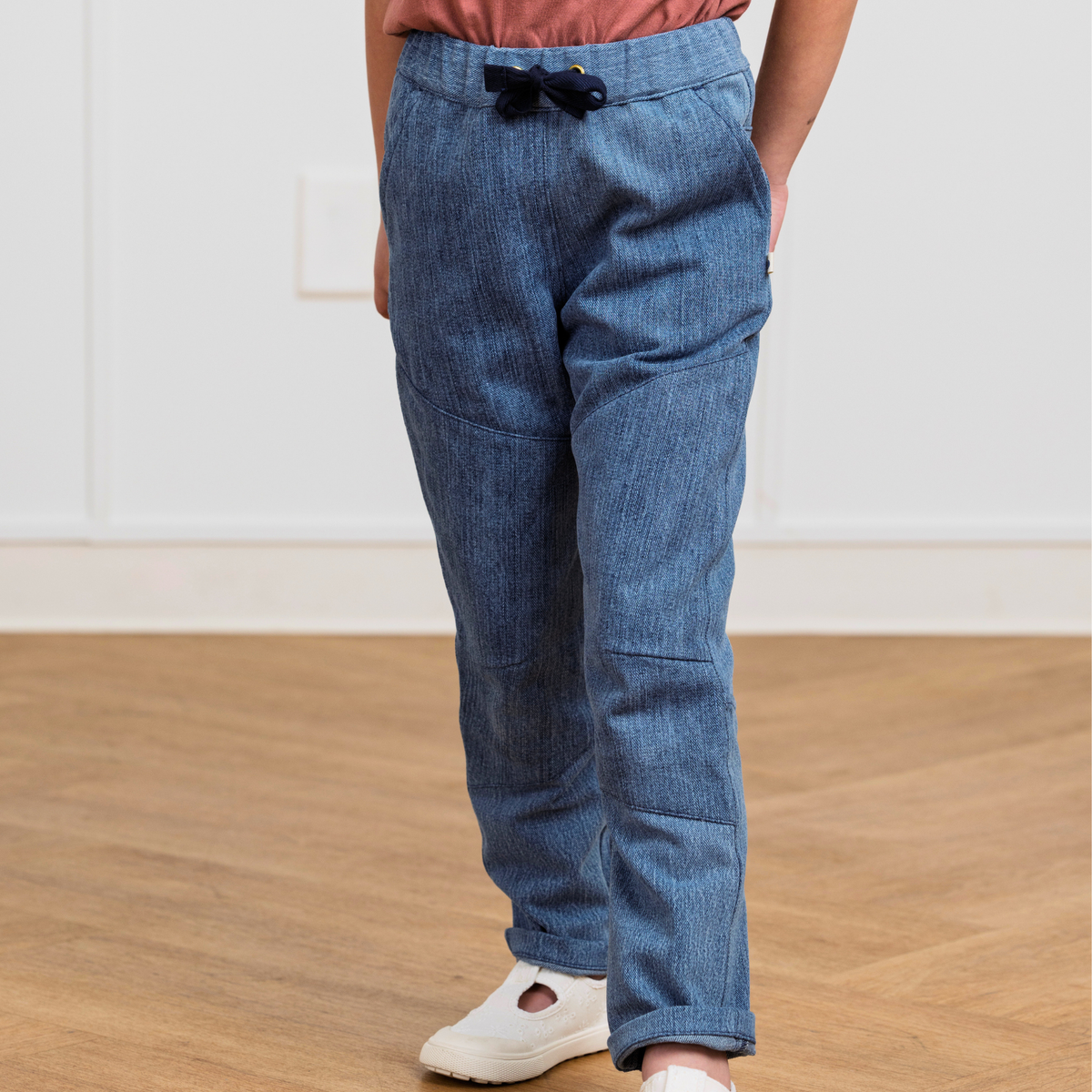 Kids' blue upcycled denim pants with drawstring waist, cuffed hems, and side pockets, paired with white sneakers