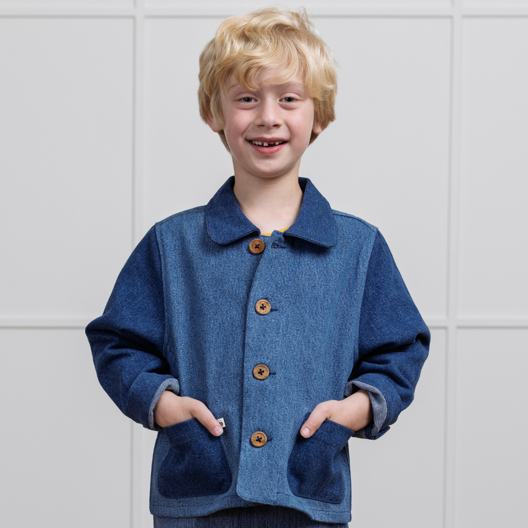 Smiling child in blue denim jacket with wooden buttons, hands in pockets, sustainable kids clothing