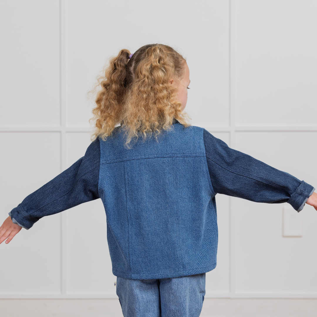 Child in blue denim jacket and jeans, back view, arms outstretched for active play