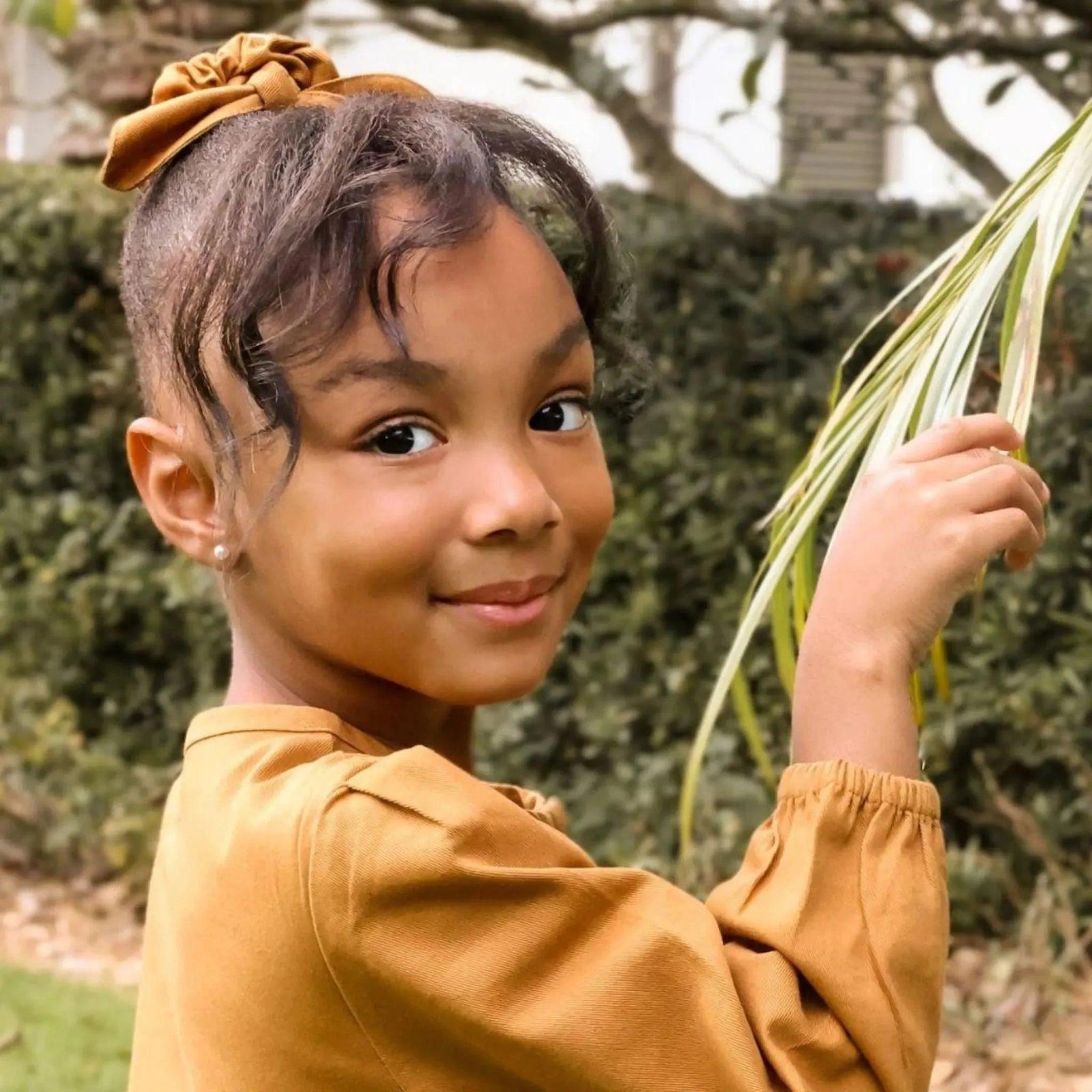 Smiling girl in sustainable Jackalo kids clothing with brown bow scrunchie outdoors