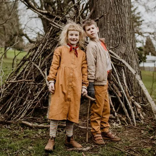 Two children happily standing next to a tree
