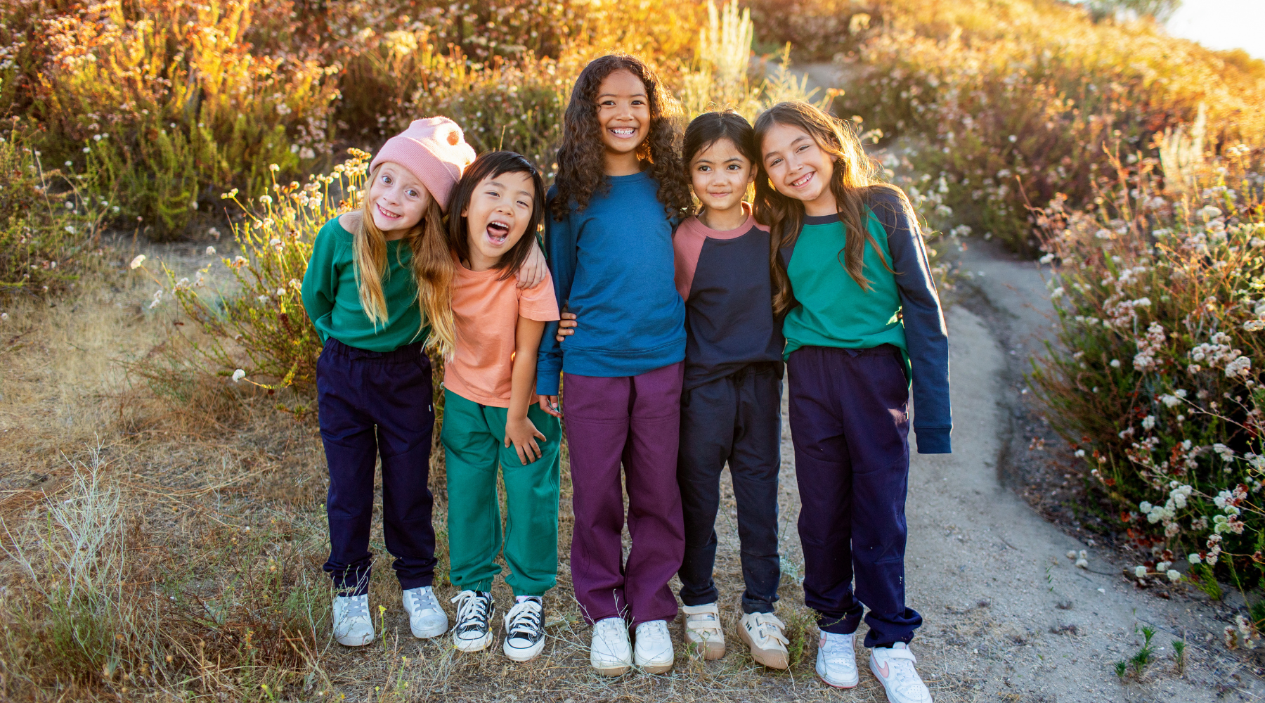 Five young girls in bright outfits smiling and standing together