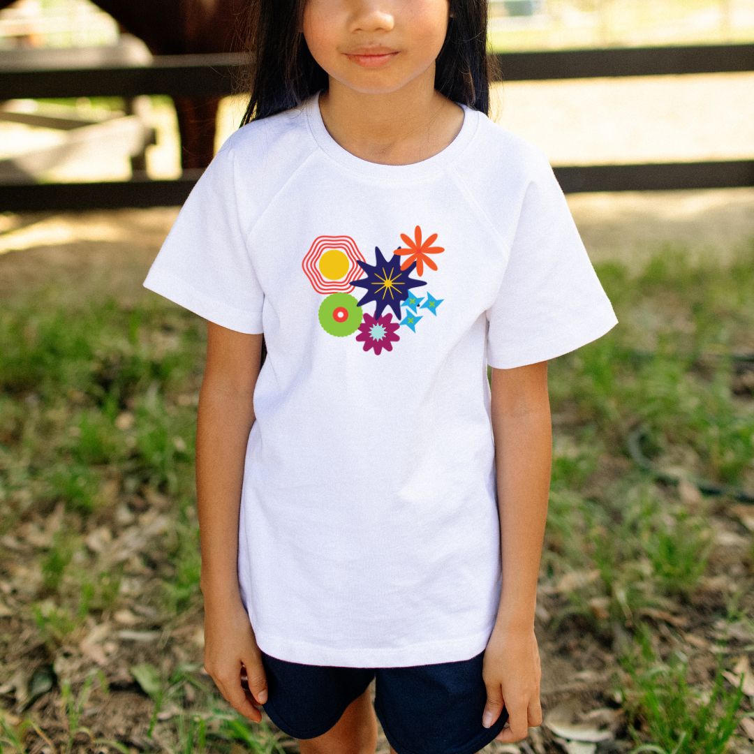 Child wearing a white t-shirt with colorful geometric designs outdoors.