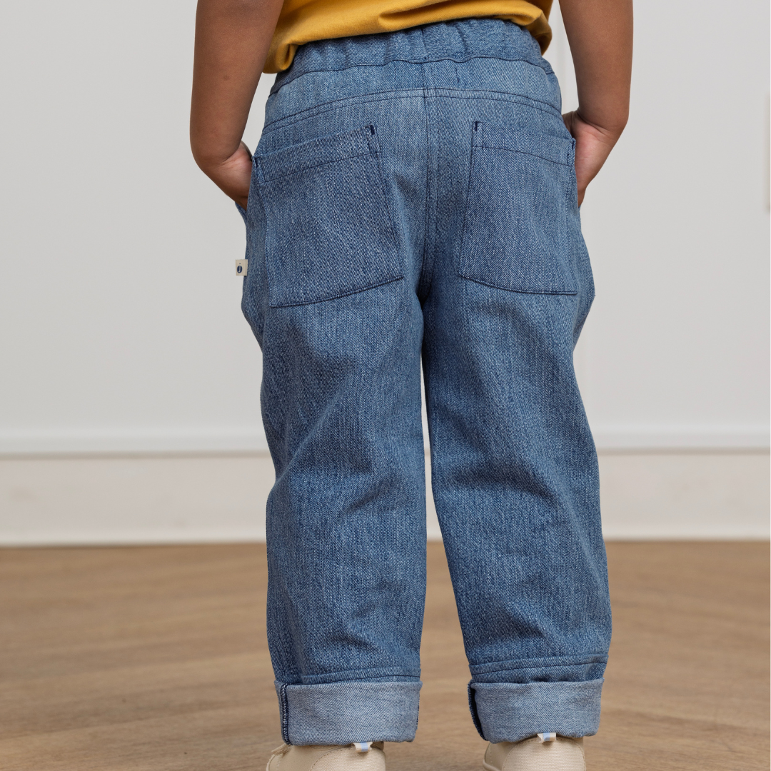 Kid wearing durable blue denim pants with back pockets, rolled cuffs, and hands in pockets for active play