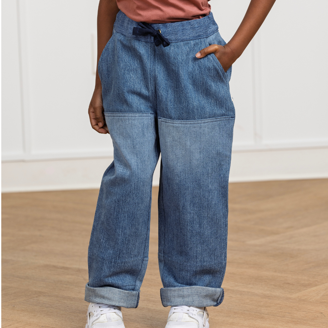 Kids' blue denim-style joggers with drawstring waist, cuffed hems, and side pockets, paired with white sneakers.