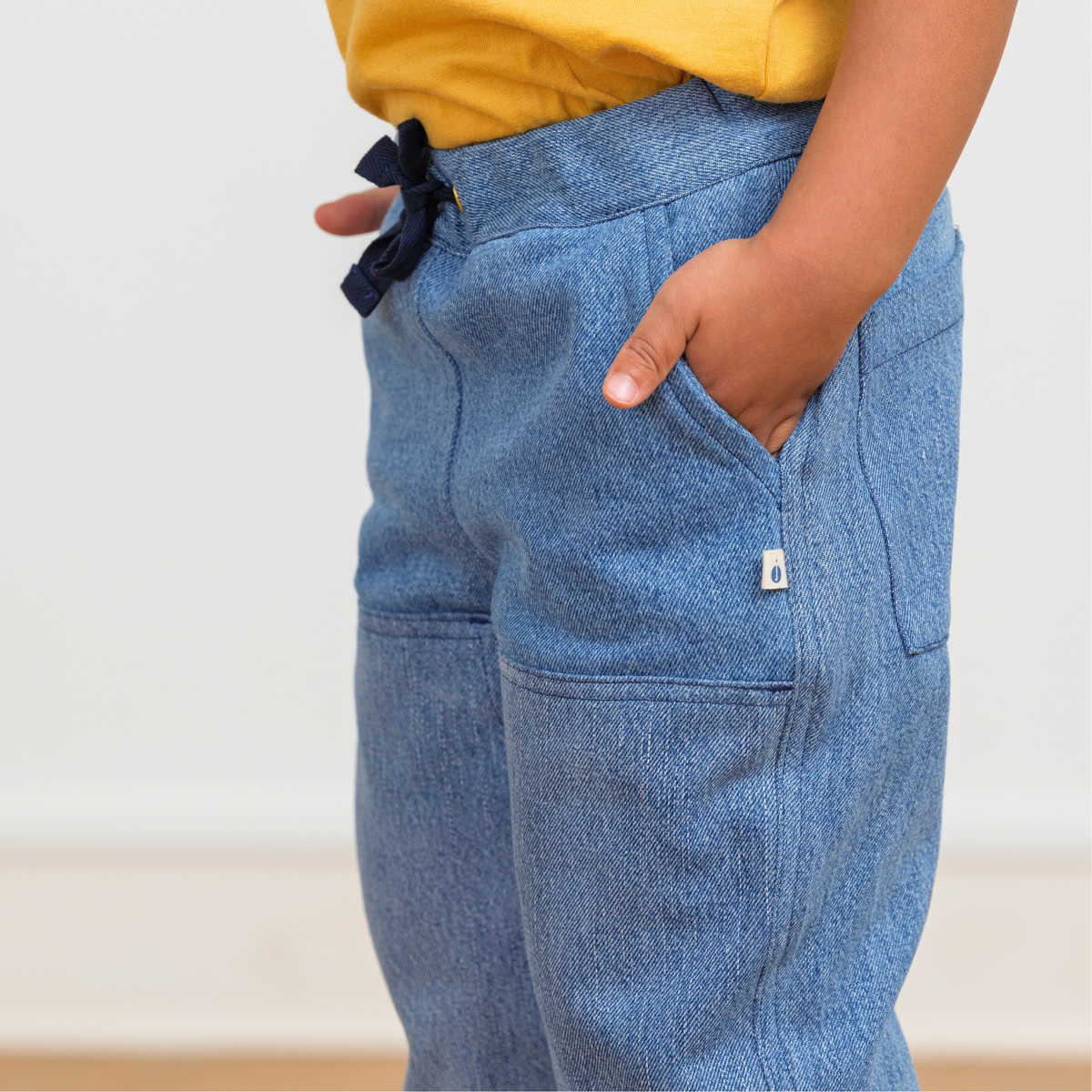 Child wearing blue upcycled denim pants with drawstring waist and side pockets, paired with yellow top