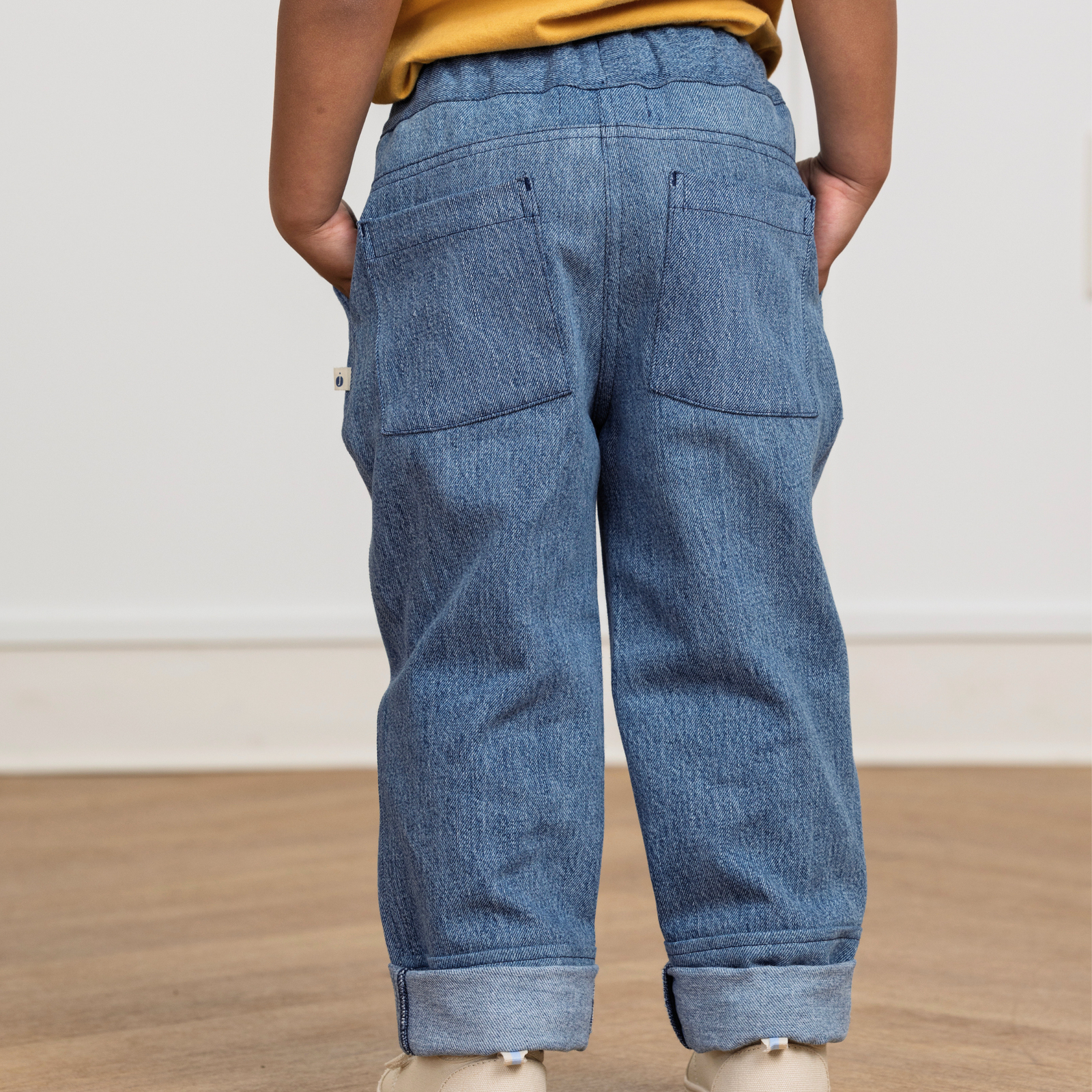 Kid wearing durable blue denim pants with back pockets, rolled cuffs, and hands in pockets for active play