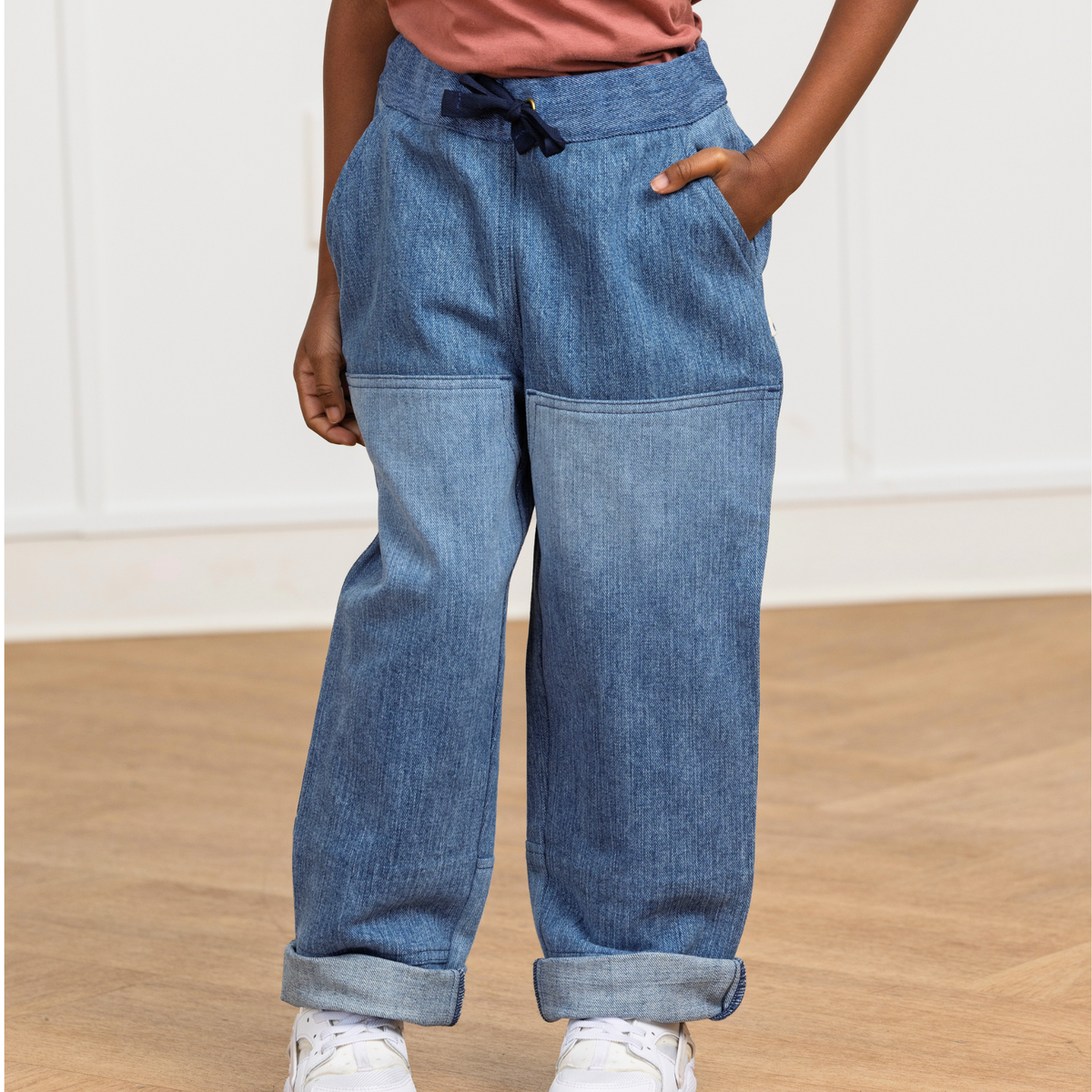 Kids' blue upcycled denim pants with drawstring waist, cuffed hems, and side pockets, paired with white sneakers.