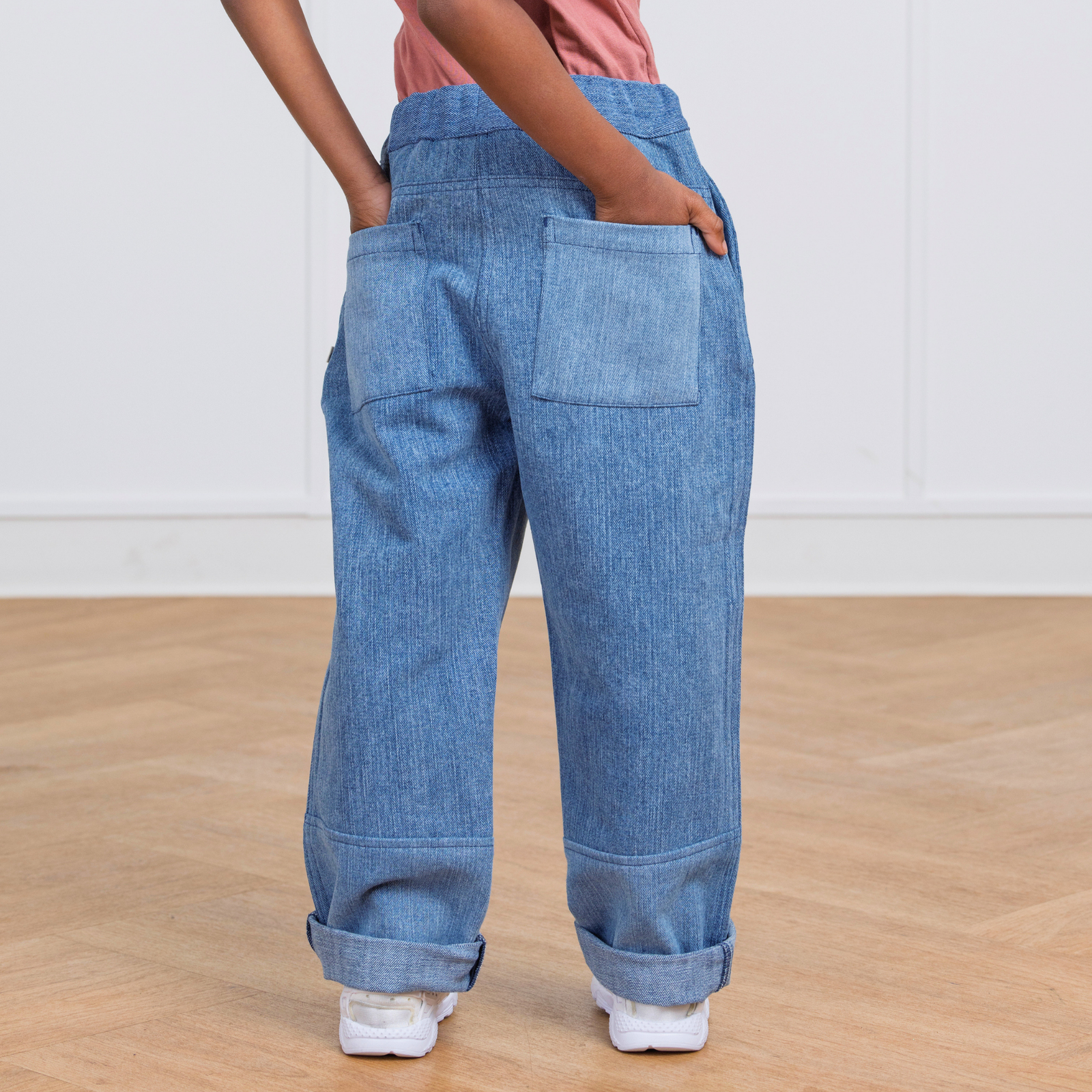 Kids' blue upcyled denim pantswith drawstring waist, cuffed hems, and side pockets, paired with white sneakers.