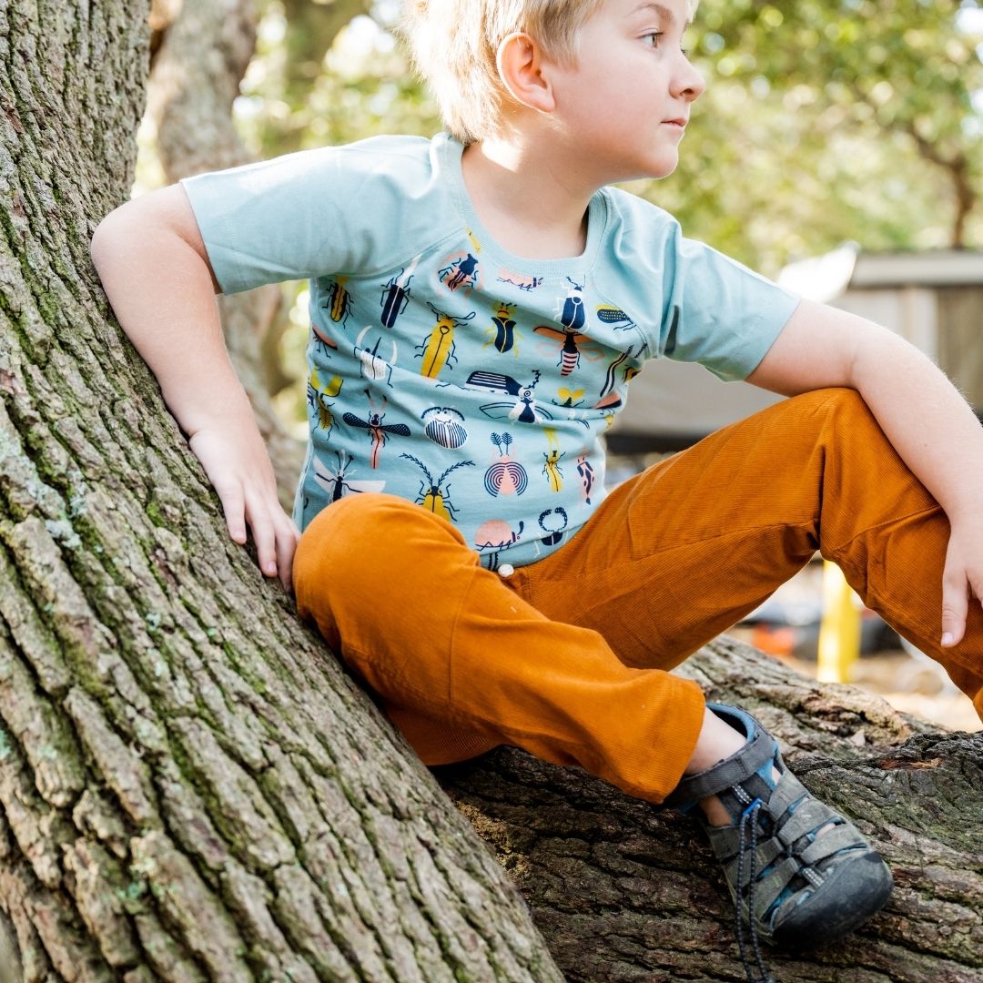 Child dressed in Jackalo sustainable clothes for kids: rust corduroy pants and Beetle Mania bug print shirt