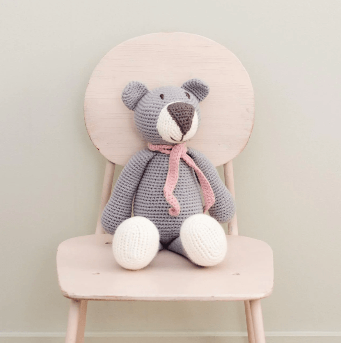 A cute crocheted teddy bear sitting on a pink chair