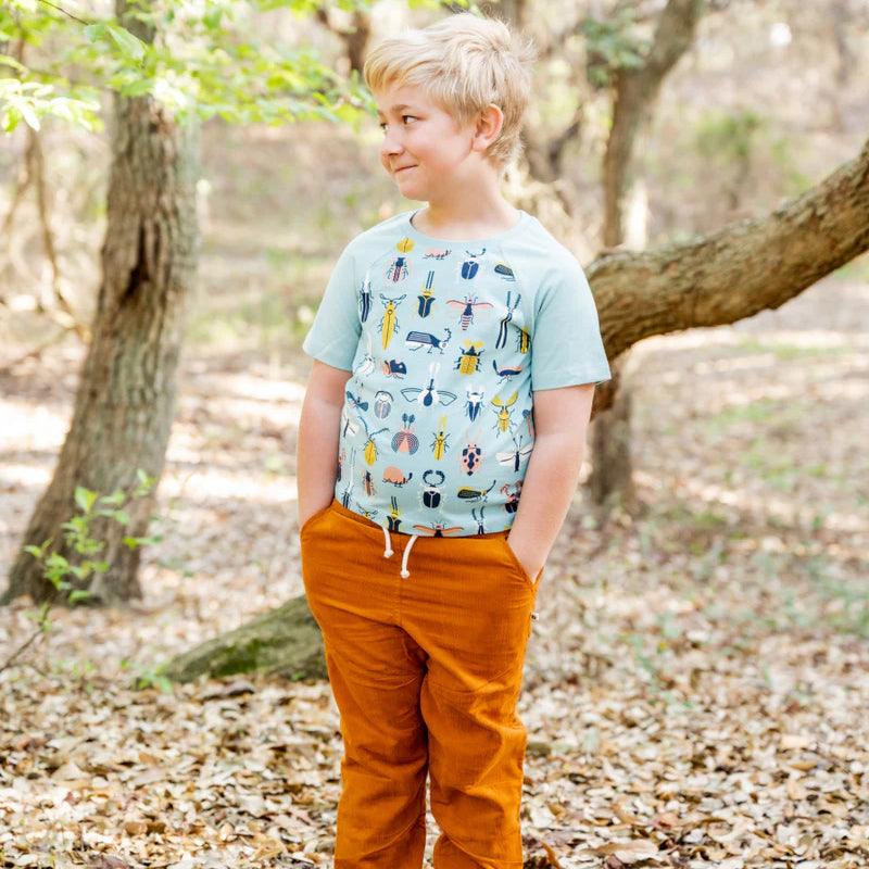 Smiling male kid wearing sky blue printed beetle shirt and orange pants
