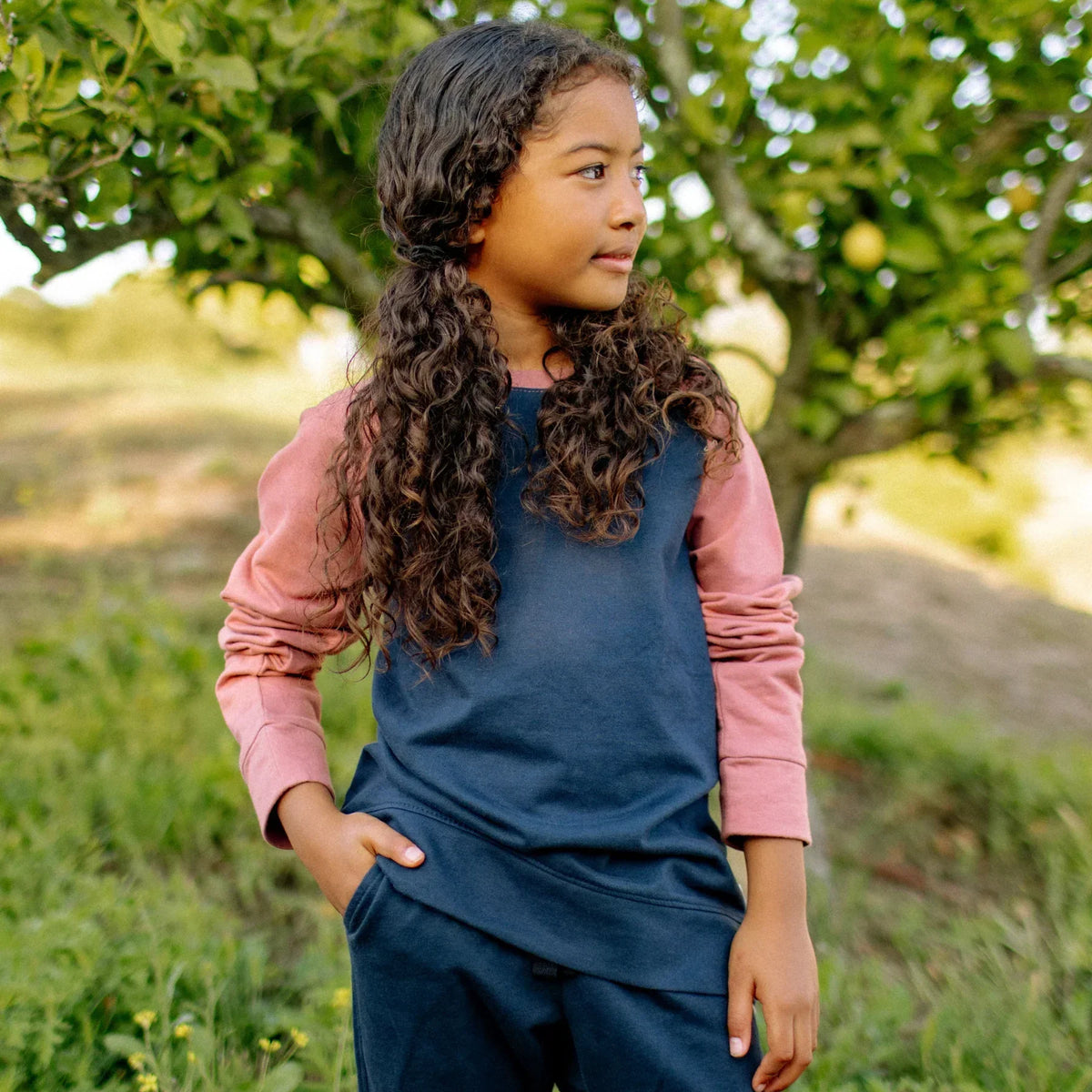 Child wearing Jackalo sustainable colorblock sweatshirt outdoors, navy and rose, by fruit trees