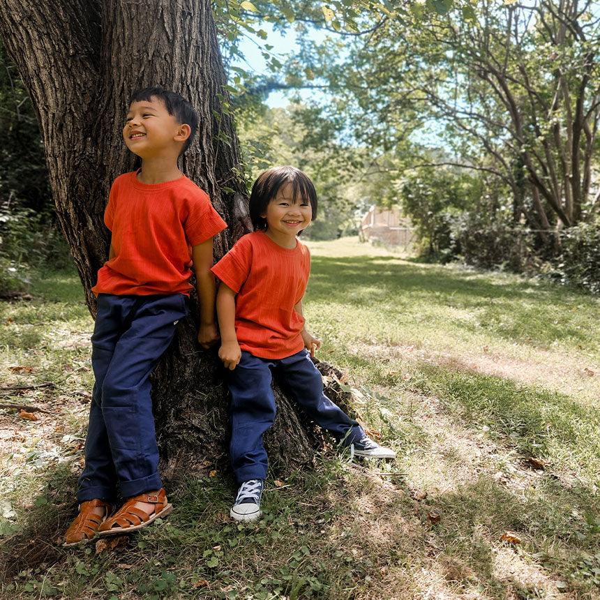 Two boys in red shirts sitting on a tree