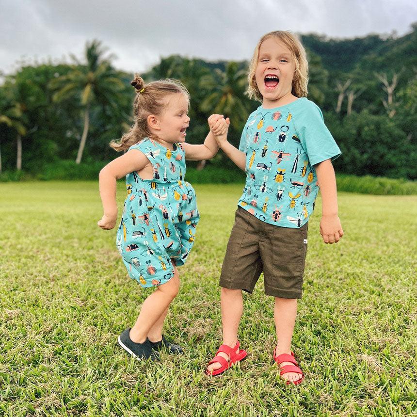 Two kids in blue shirts and shorts standing in a field of grass