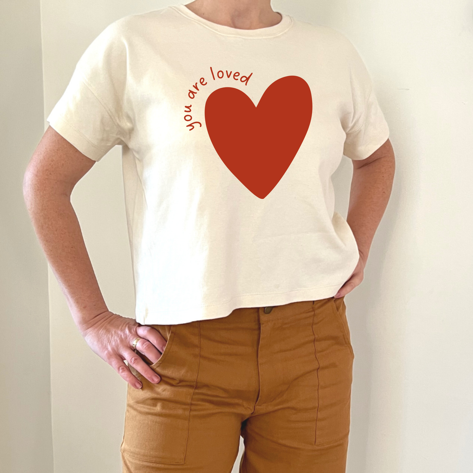 Cream t-shirt with red heart and 'you are loved' text, paired with tan pants