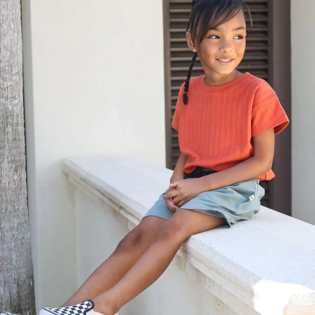 Young girl wearing red shirt and teal shorts